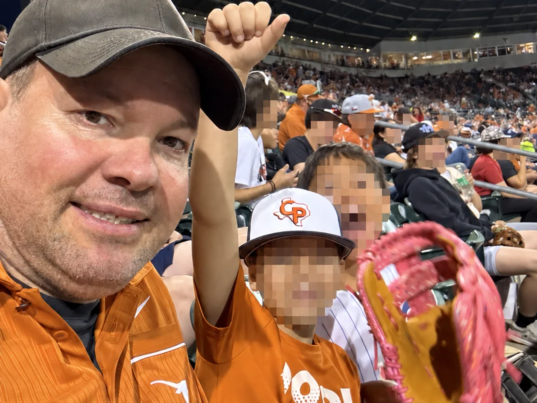Mark with two children at a Texas Longhorns baseball game; the children and young spectators’ faces are obscured for privacy