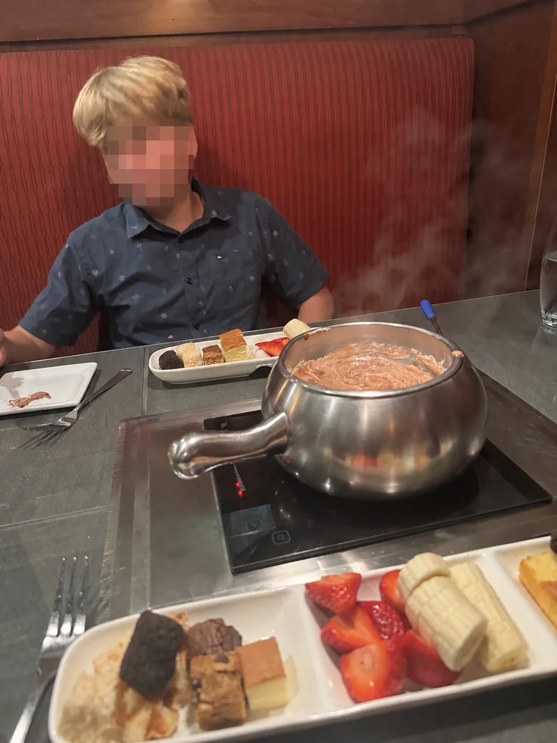 A child enjoying chocolate fondue and fruit at The Melting Pot; the child’s face is obscured for privacy